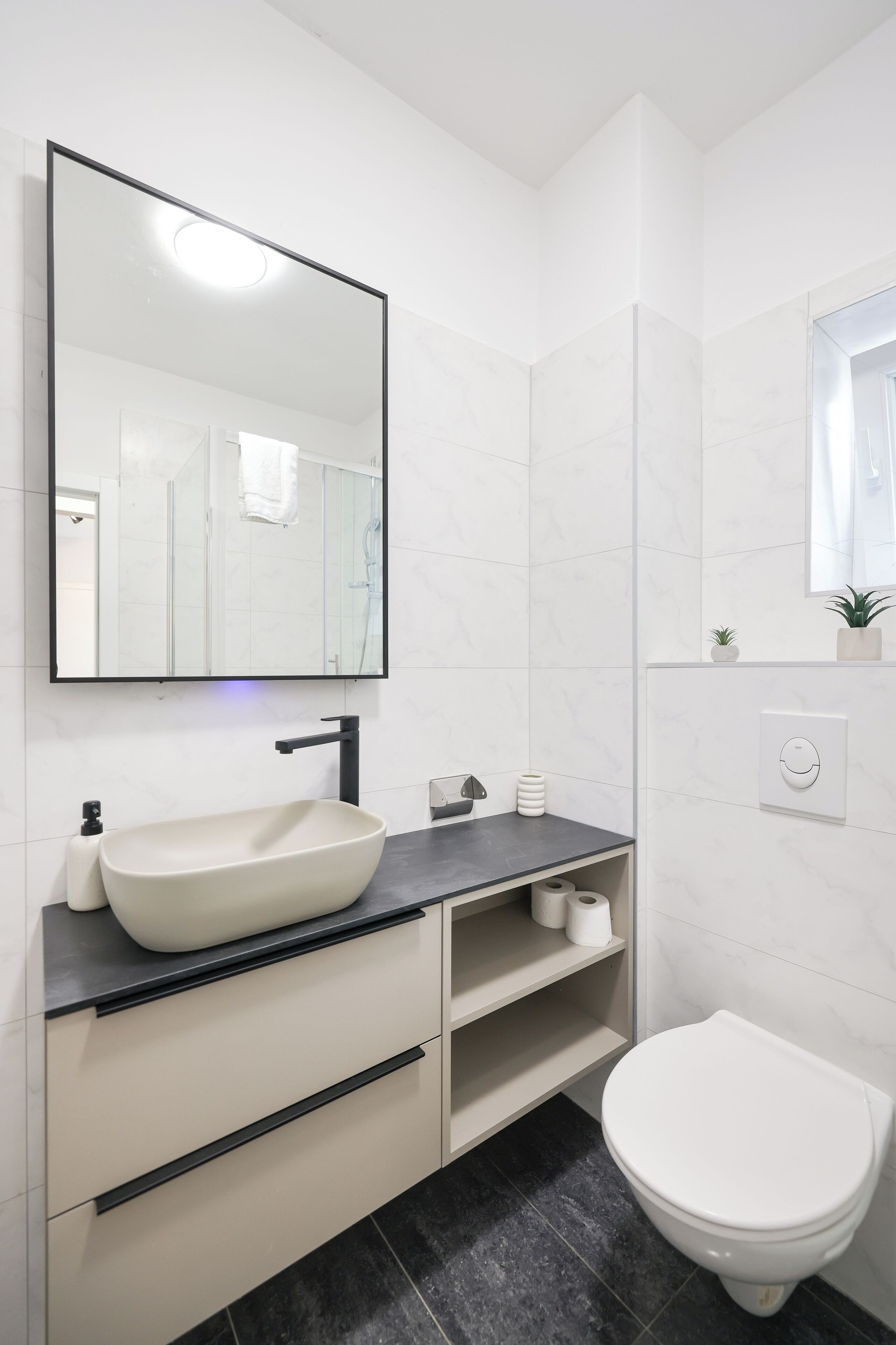 Un baño moderno con un espejo grande, un lavabo sobre encimera, inodoro y zona de ducha.