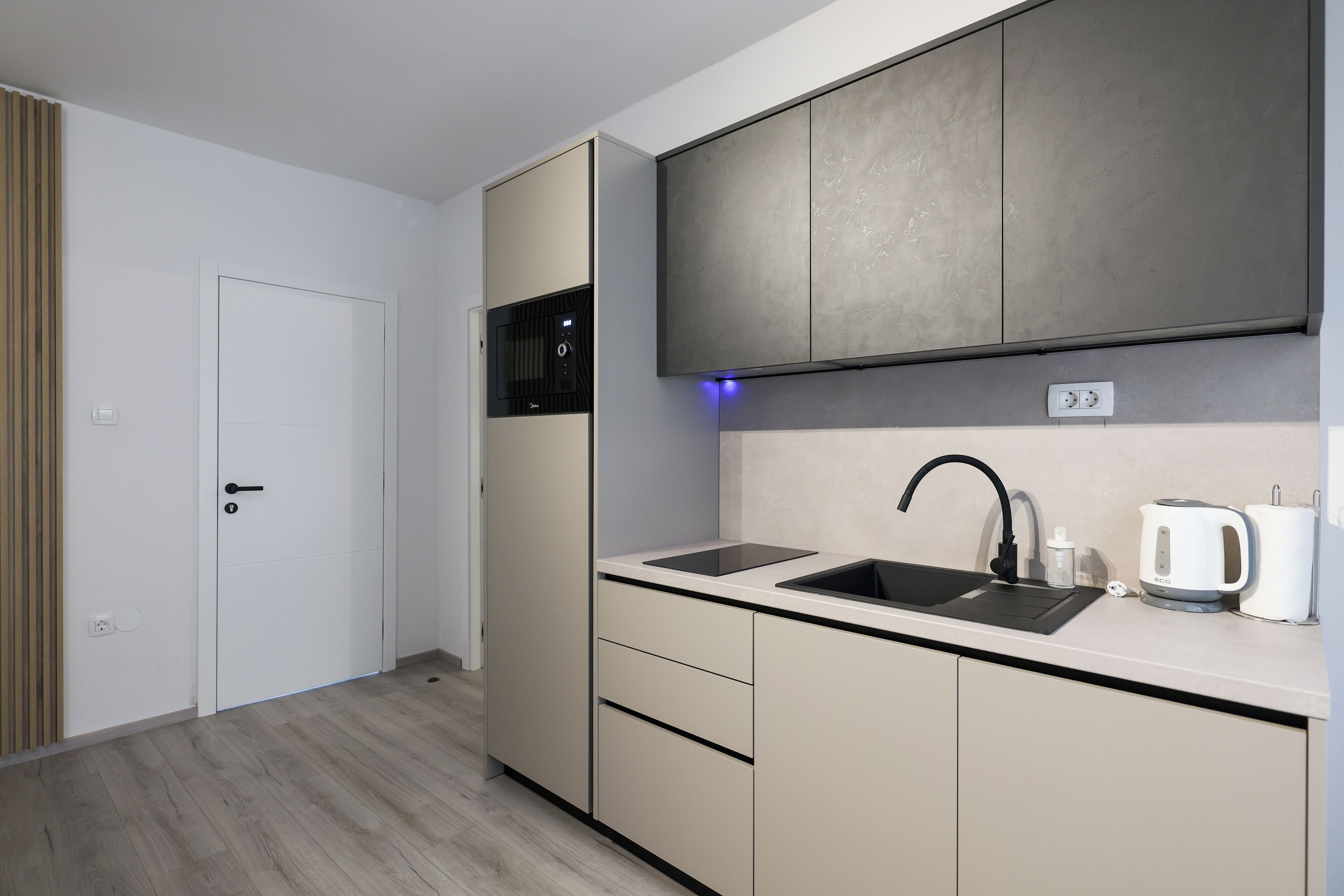 Una cocina moderna con horno empotrado, un lavamanos y un hervidor sobre la encimera.