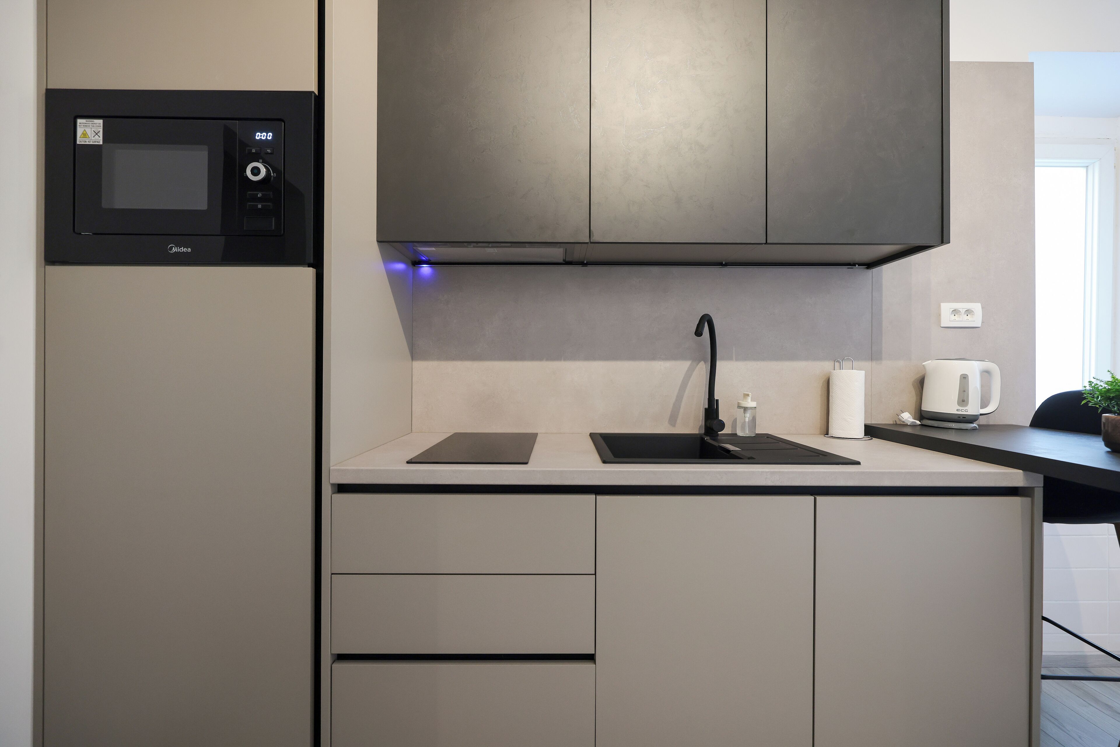 A modern kitchen with a built-in microwave, a sink, and a kettle.