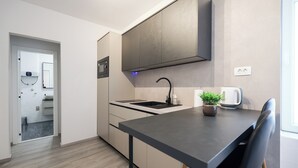 Et moderne køkken med en mørk bordplade, en vask og en mikrobølgeovn. Der står en potteplante på bordet og en elkedel.