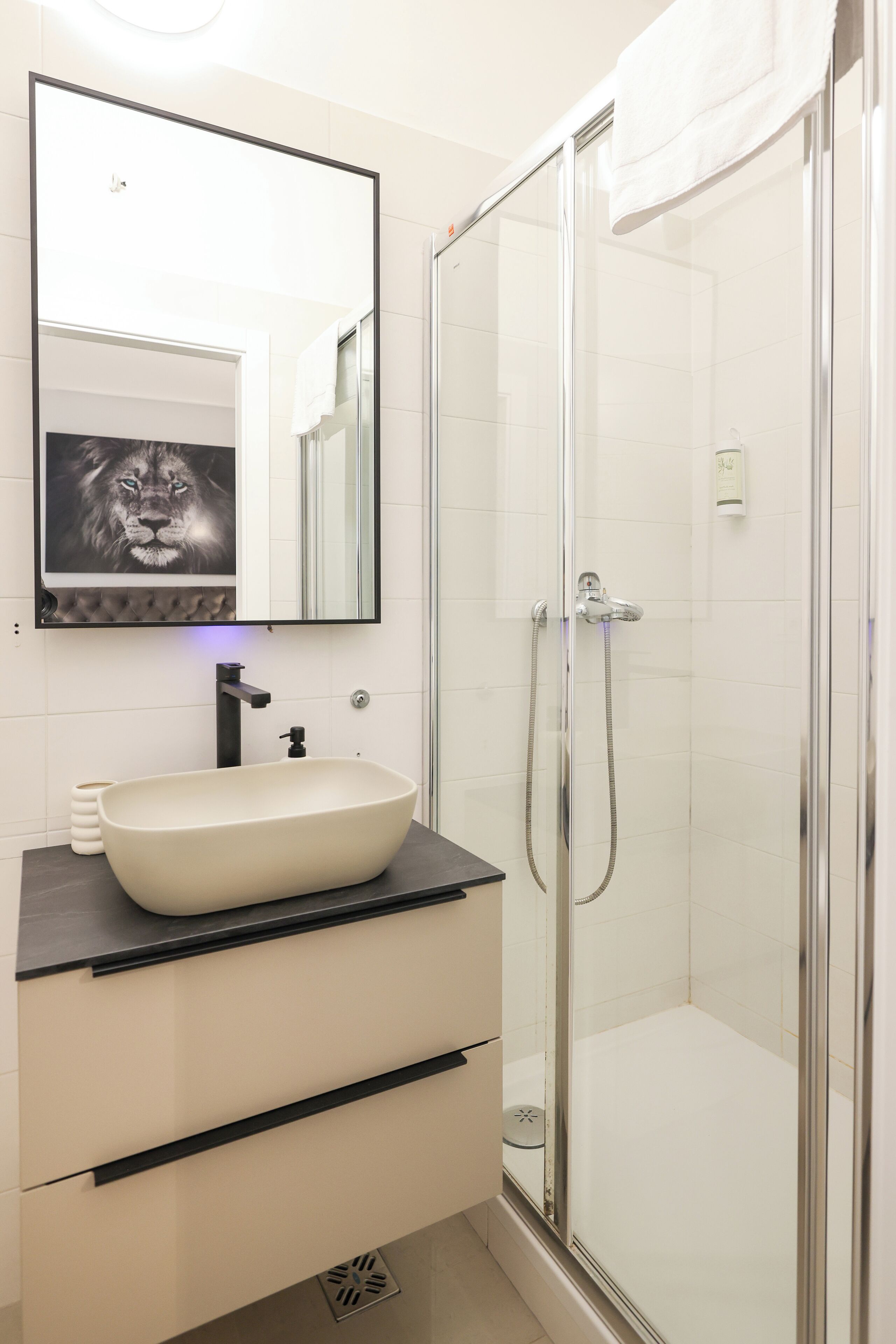 Un baño con un espejo grande, un lavamanos tipo recipiente, un box de ducha y una toalla colgada en la puerta.