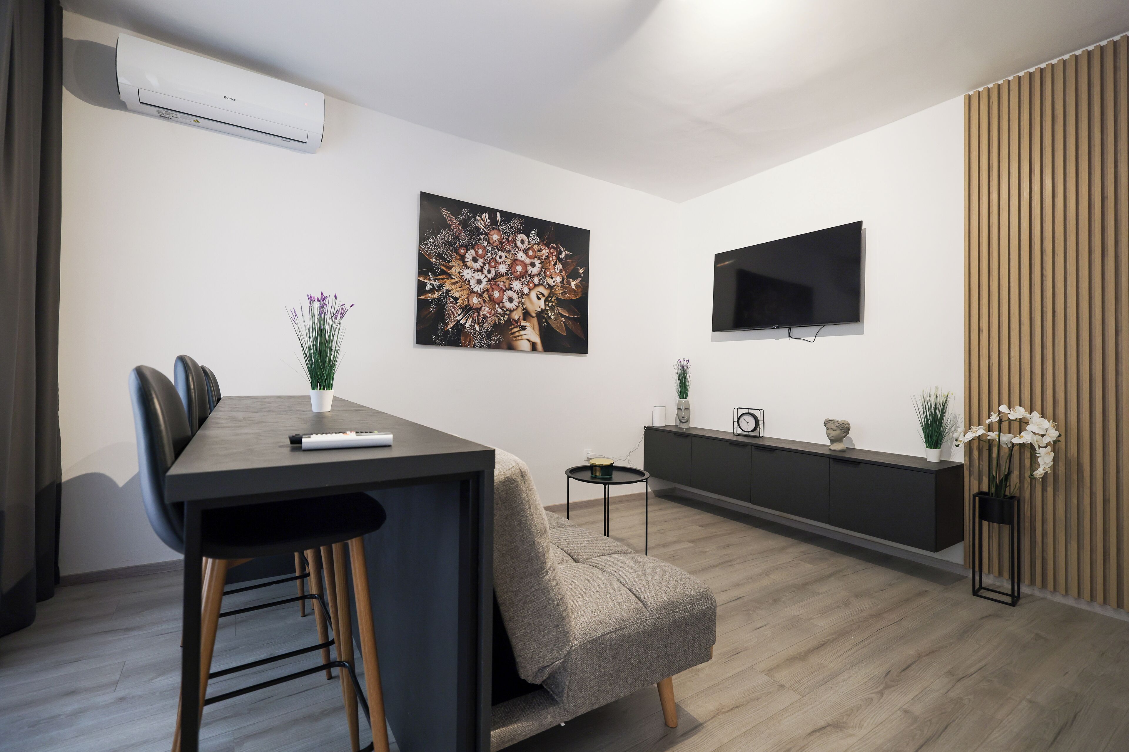 Una sala de estar moderna con comedor, un televisor de pantalla plana montado en la pared y una planta en maceta.