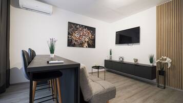 Una sala de estar moderna con comedor, un televisor de pantalla plana montado en la pared y una planta en maceta.