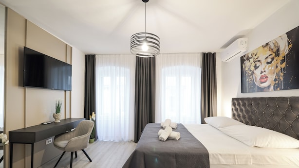 Et moderne hotelværelse med seng, skrivebord, stol, fjernsyn og et stort vindue med gardiner.