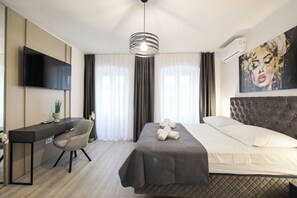 Una habitación de hotel moderna con cama, escritorio, silla, televisor y un ventanal con cortinas.