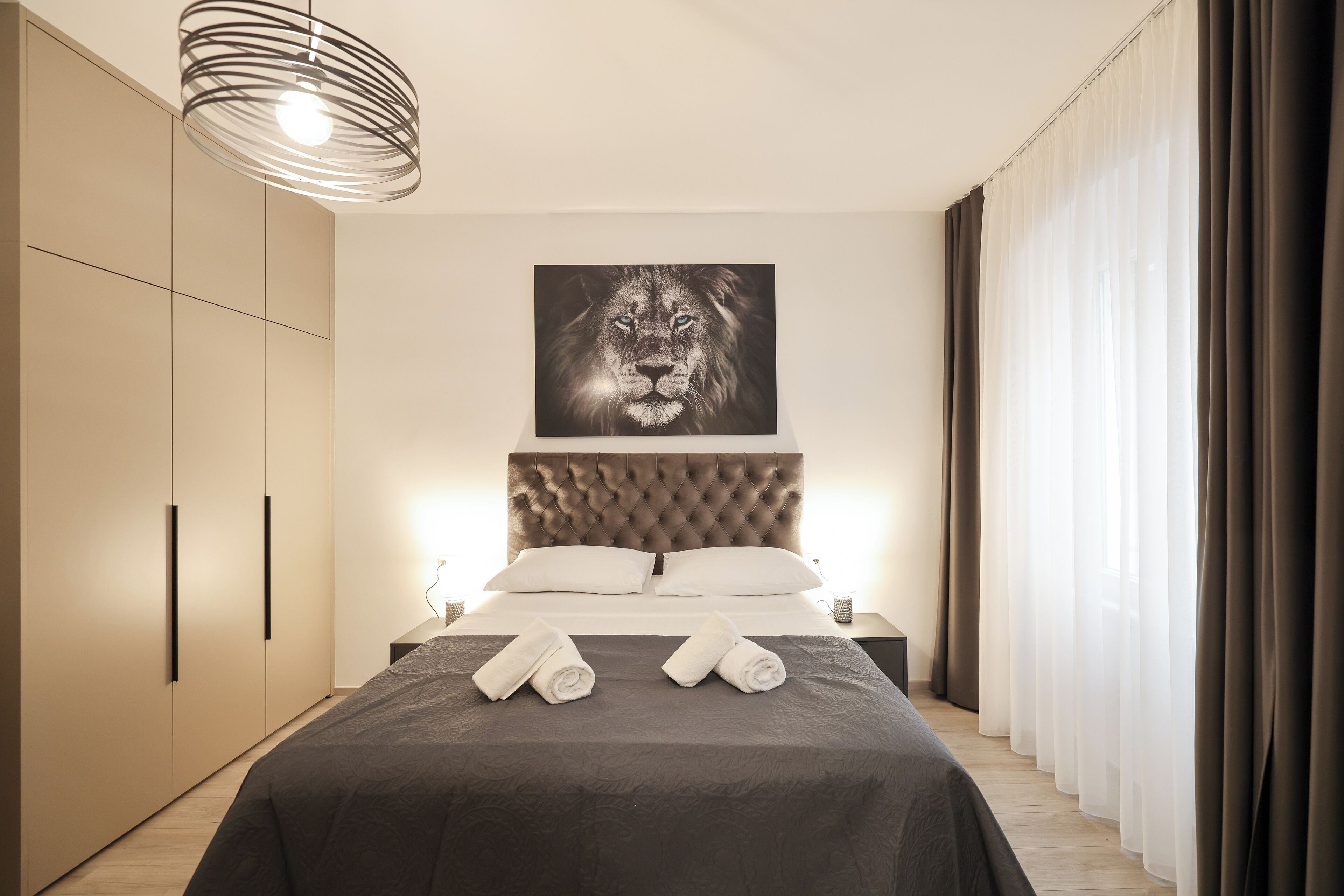 Een moderne slaapkamer met een groot bed, een gestuikt hoofdeinde en een afbeelding van een leeuw erboven.