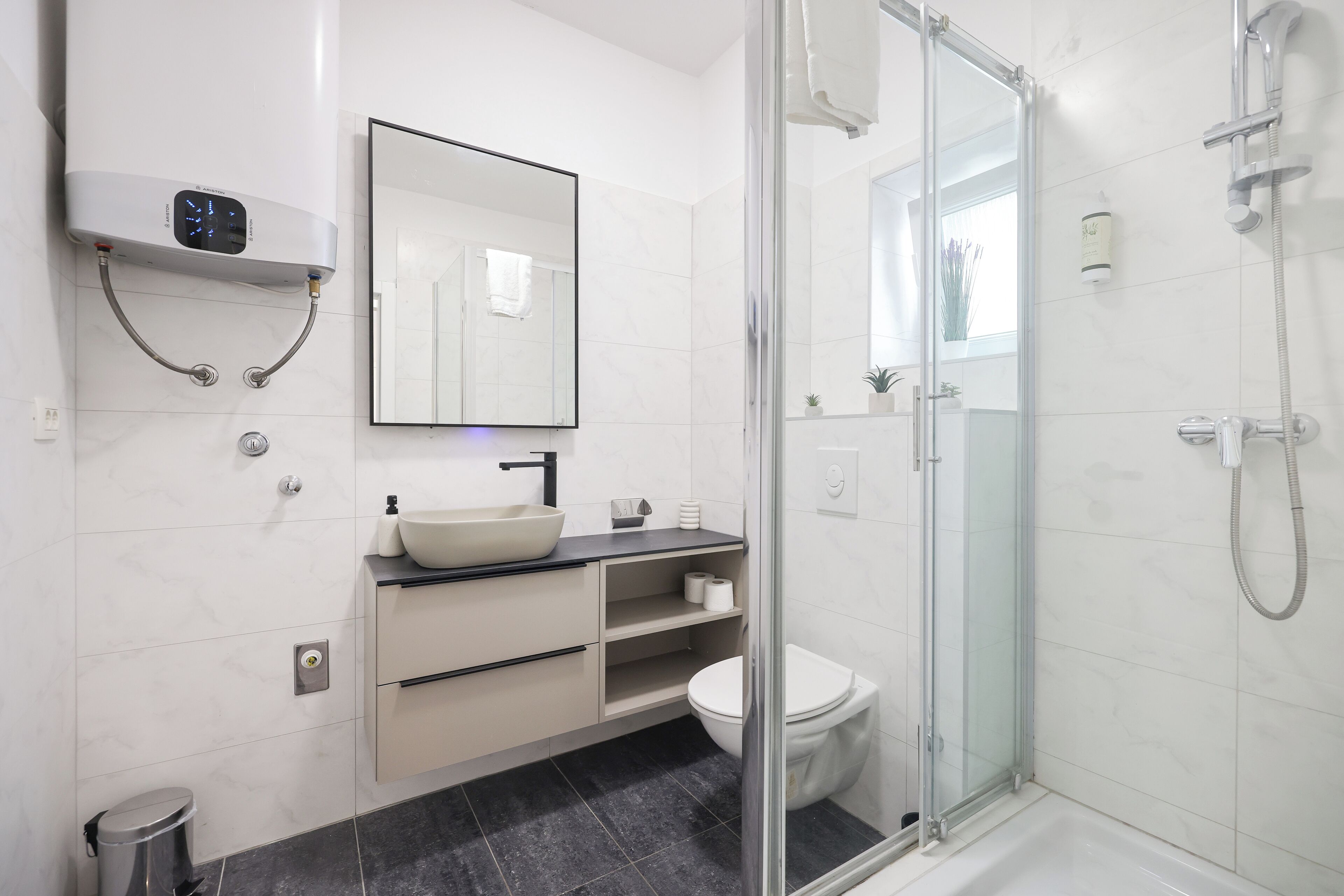 Un baño moderno con ducha de vidrio, lavamanos blanco y retrete.