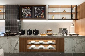A modern kitchen with marble countertops, a coffee machine, and a coffee station. There are two chalkboard signs on the wall and wooden shelves above the counter. - UC by Hyatt  West Railway St Hotel (Tianjin)