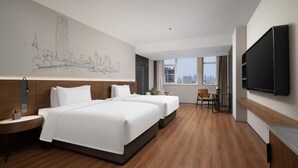 Habitación de hotel con dos camas, un televisor de pantalla plana, un mural con un paisaje urbano y vistas de la ciudad a través de amplias ventanas.