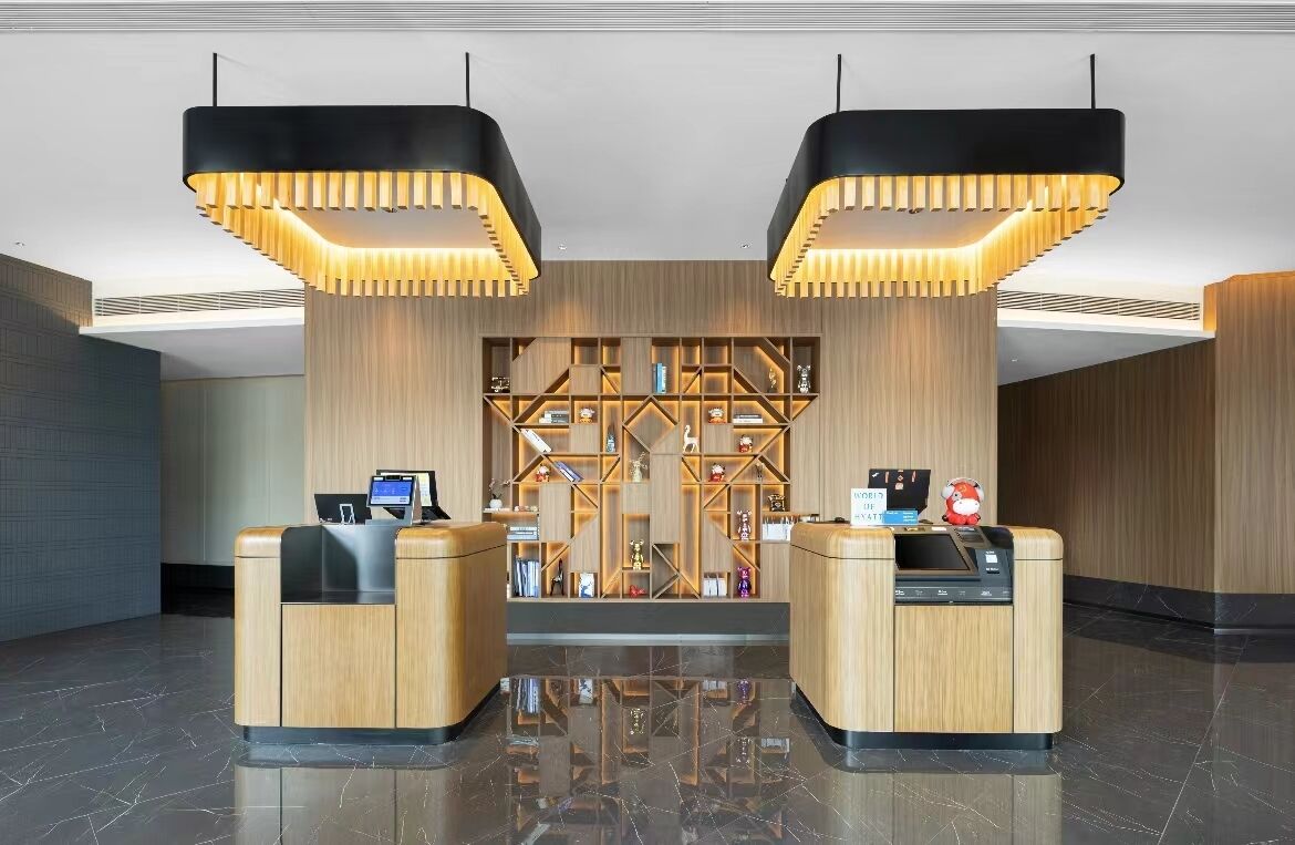 A modern reception area with two wooden reception desks, a central display wall with various items, and pendant lighting.