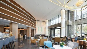 Un moderno vestíbulo de hotel con techo curvo, una zona de estar central y grandes ventanales que ofrecen vistas de la ciudad.