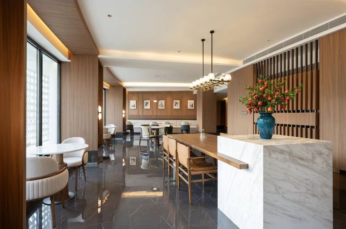 A modern hotel lobby with a marble reception desk, wooden panel walls, and a large vase of flowers.