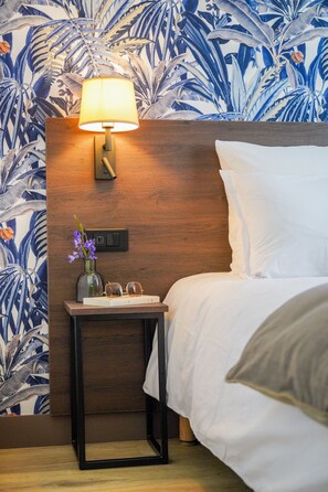 Une chambre d’hôtel avec une tête de lit en bois, une table de chevet avec une lampe, un vase de fleurs et un lit avec du linge de lit blanc.