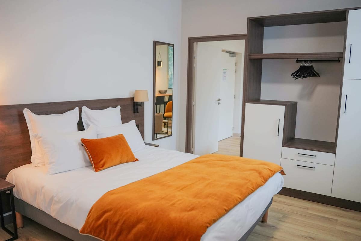 A hotel room with a bed, a nightstand, a lamp, a mirror, and a wardrobe.