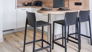 Una cucina moderna con mobili bianchi, forno a microonde integrato, cappa aspirante nera e piano di lavoro in legno. Sono presenti tre sgabelli da bar neri e un lampadario.