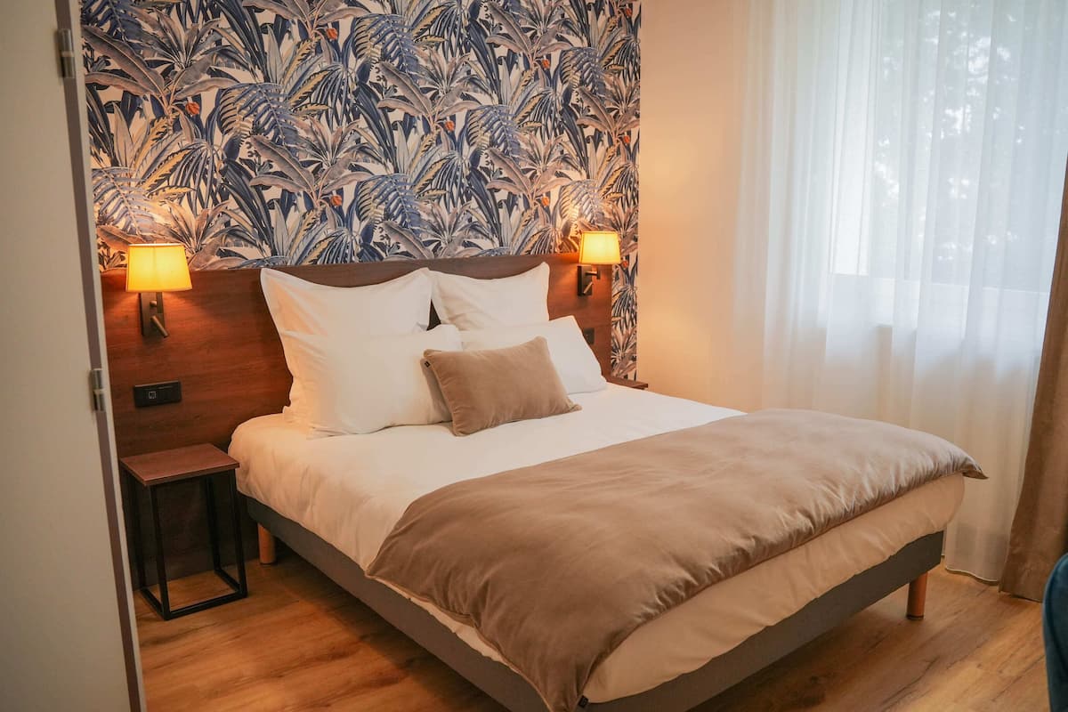A hotel room with a large bed, two bedside lamps, a wooden headboard, and a patterned wallpaper.