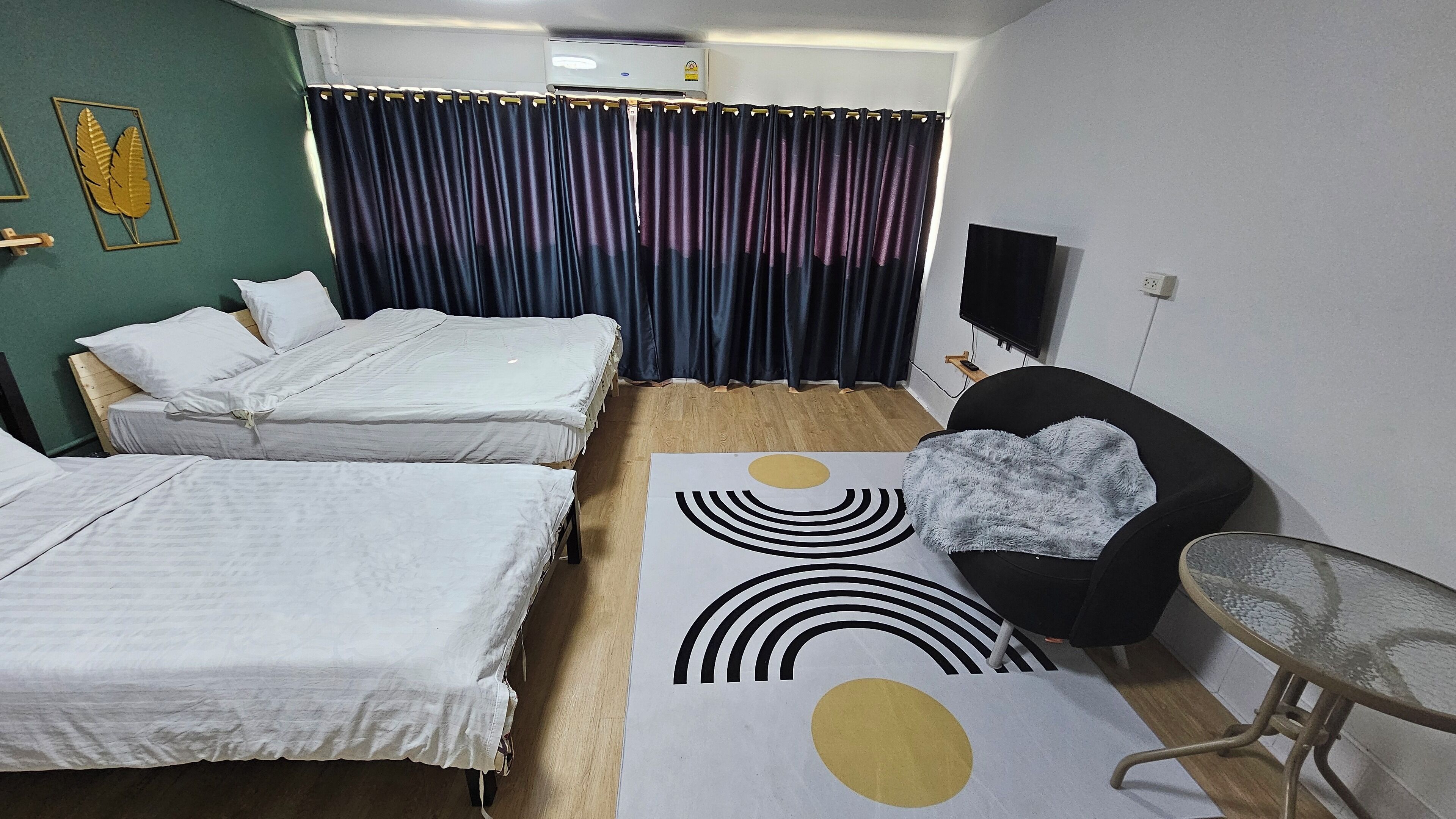 A hotel room with two single beds, a sofa, a small table, a TV, and a curtain.
