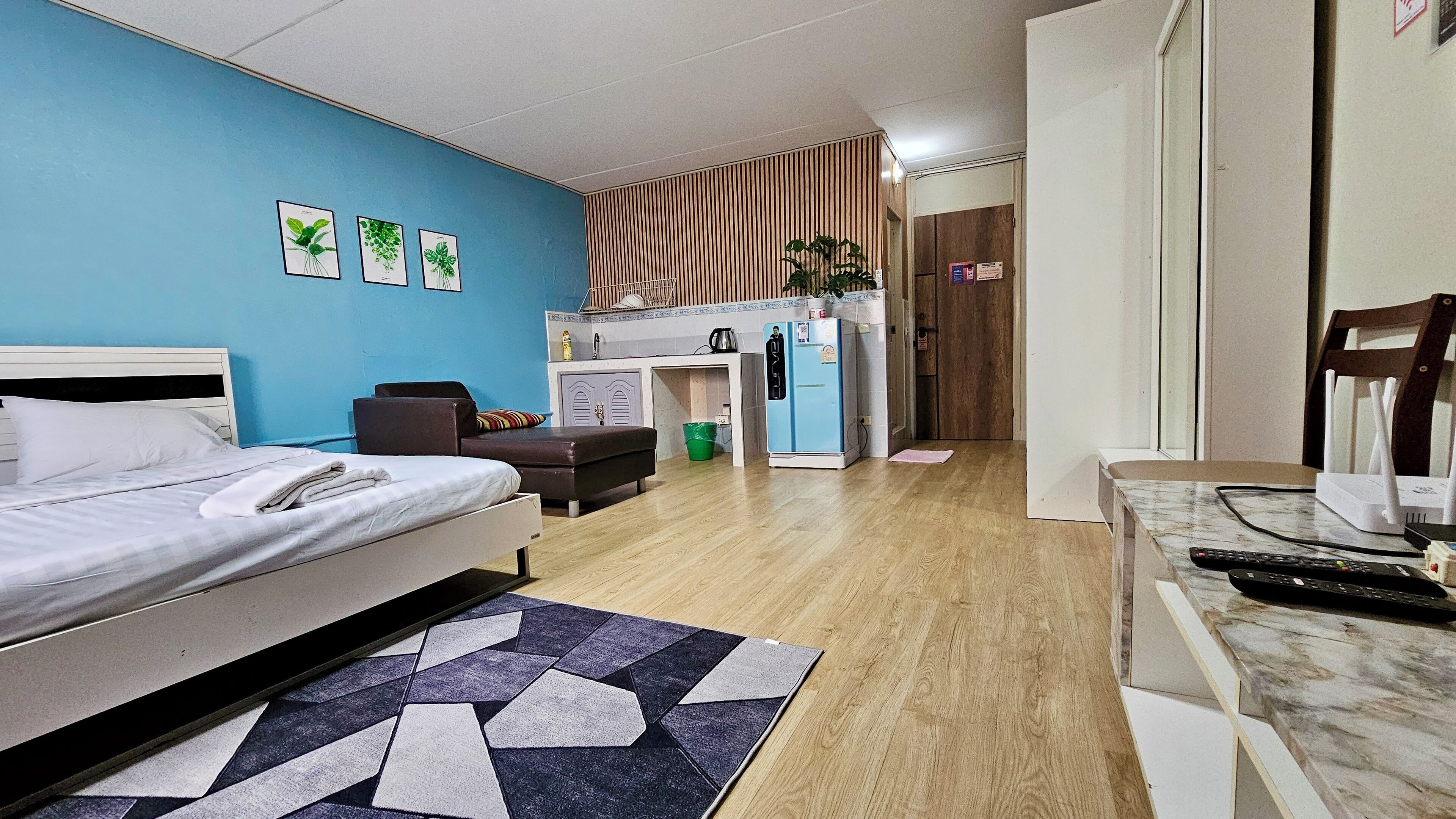 A hotel room with a bed, a desk, a chair, a small kitchenette, and a bathroom.