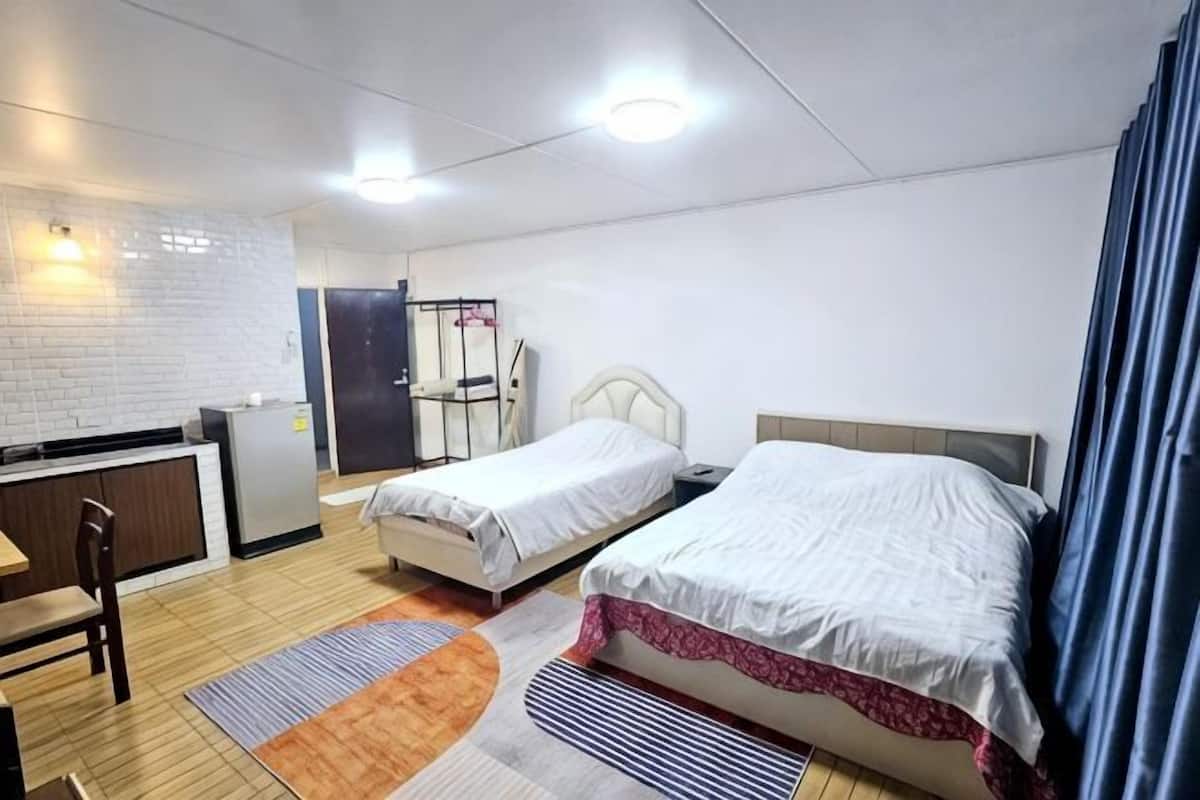 A hotel room with two beds, a desk, a chair, a small kitchenette, and a bathroom.