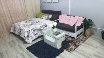 Un dormitorio con una cama, un sofá blanco, una mesa de centro de vidrio, una alfombra negra y una planta en maceta.