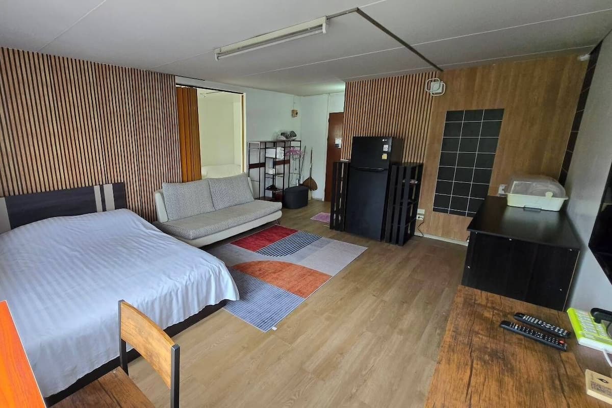 A modern hotel room with a bed, sofa, desk, and refrigerator.