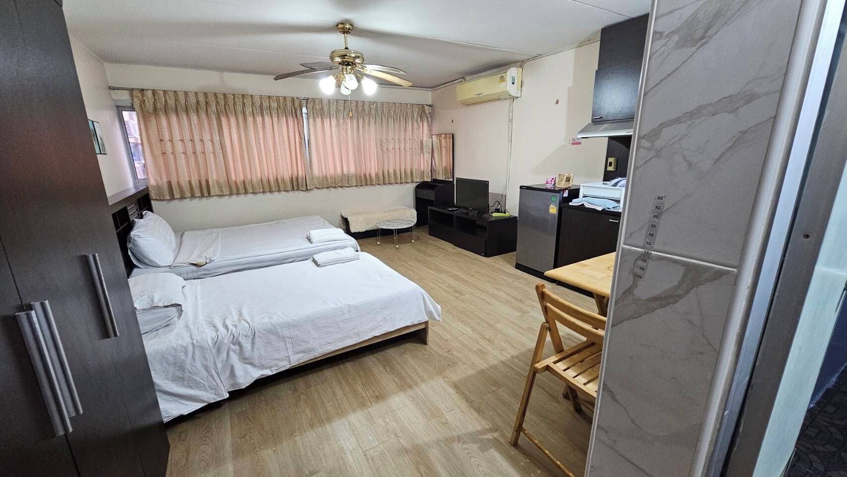 Una habitación pequeña con cama, escritorio, silla, ventilador de techo y ventana con cortinas.