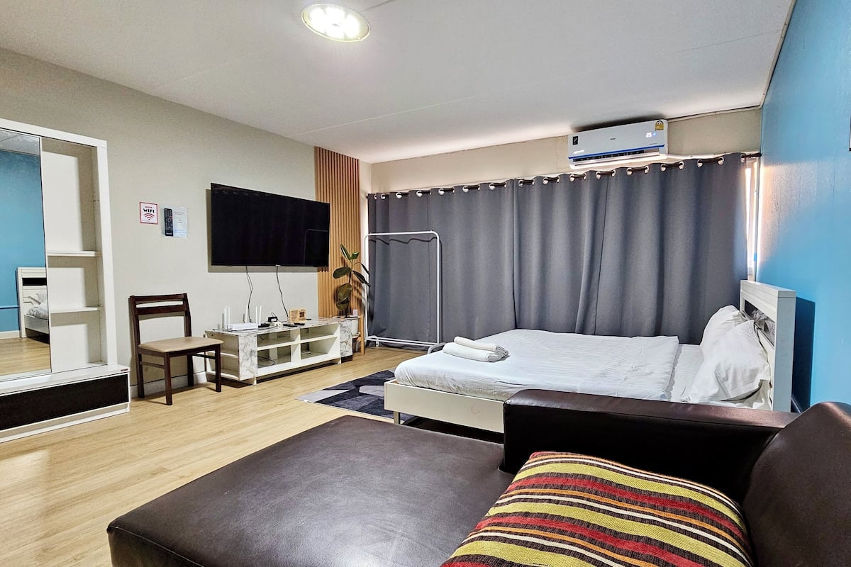 A modern hotel room with a bed, a desk, a chair, a TV, and a window with curtains.