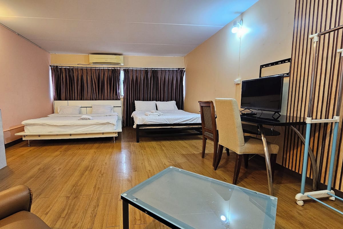 A hotel room with two beds, a desk with a computer, a TV, and a glass coffee table.