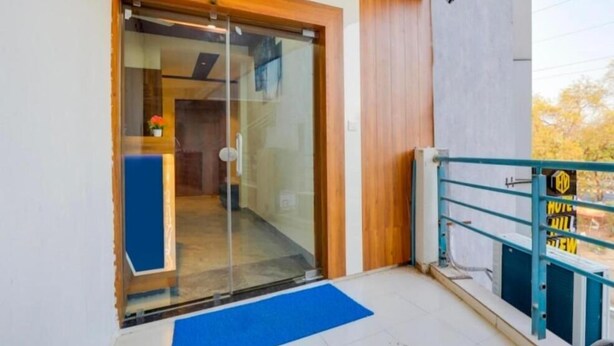 Entrada de hotel con puerta de vidrio, felpudo azul y barandilla de metal.