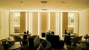 Een moderne hotel lobby met een minimalistisch ontwerp, met een zithoek met banken en tafels, een receptiebalie en een grote spiegel die de ruimte weerspiegelt.