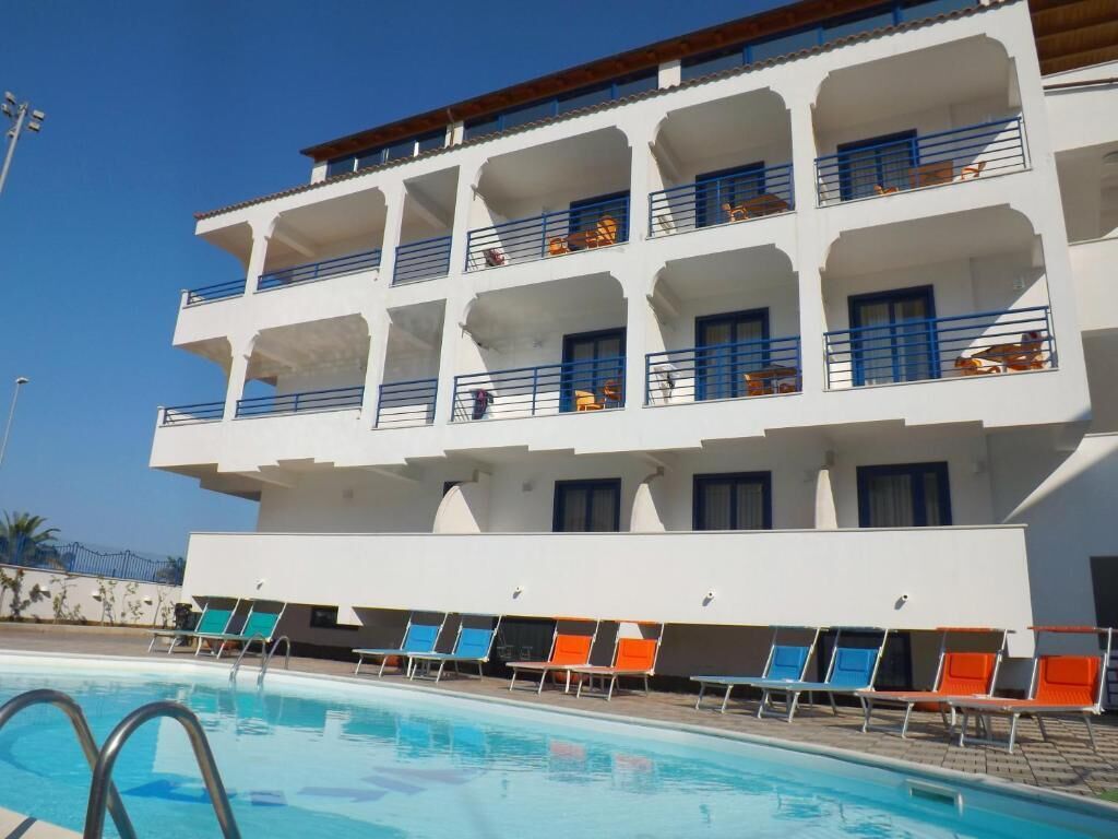 A multi-story hotel with a swimming pool and sun loungers.