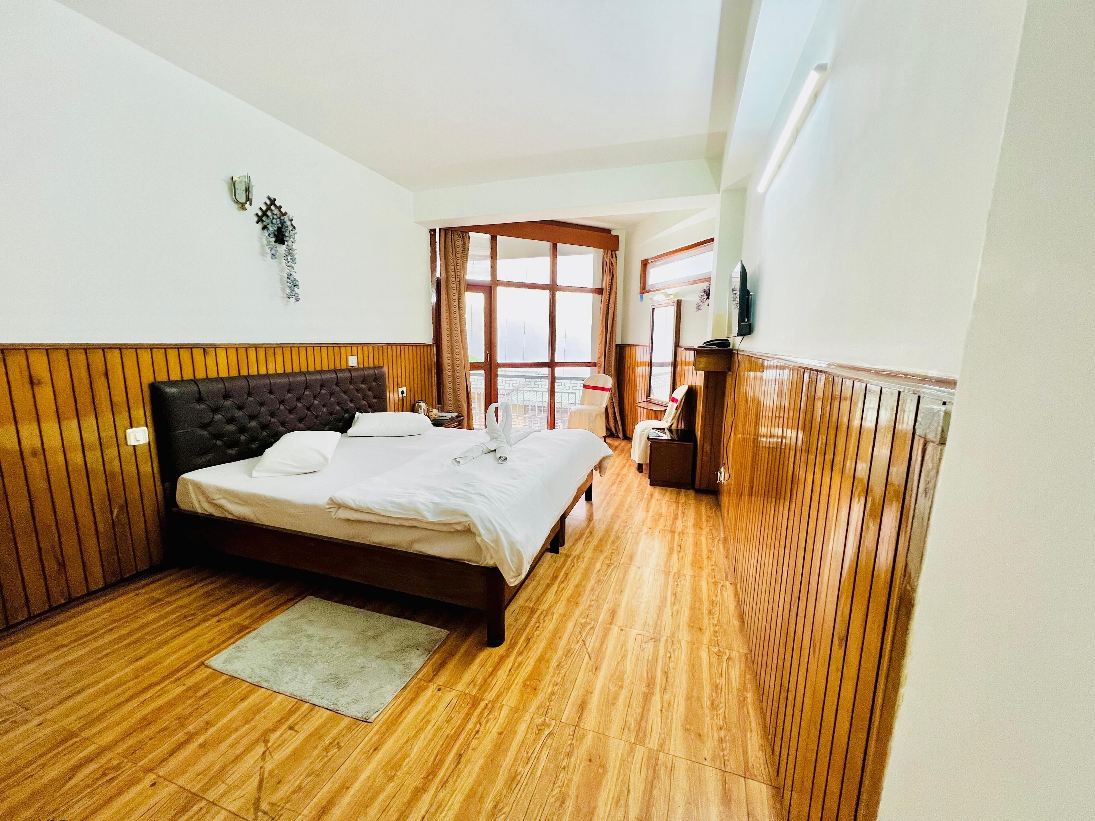 A hotel room with a wooden paneled wall, a bed with white linens, a small table, and a chair.