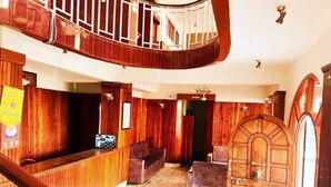 A lobby with a wooden reception desk, a staircase, and a large arched door. - HOTEL TASHI GYAL TSEN (Gyalshing)