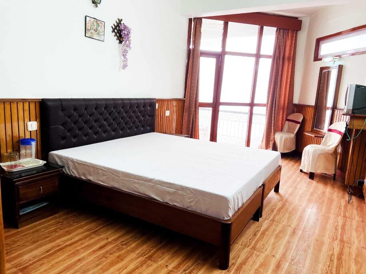 Habitación de hotel con una cama grande, paneles de madera, suelo de madera, un televisor y una ventana con cortinas.