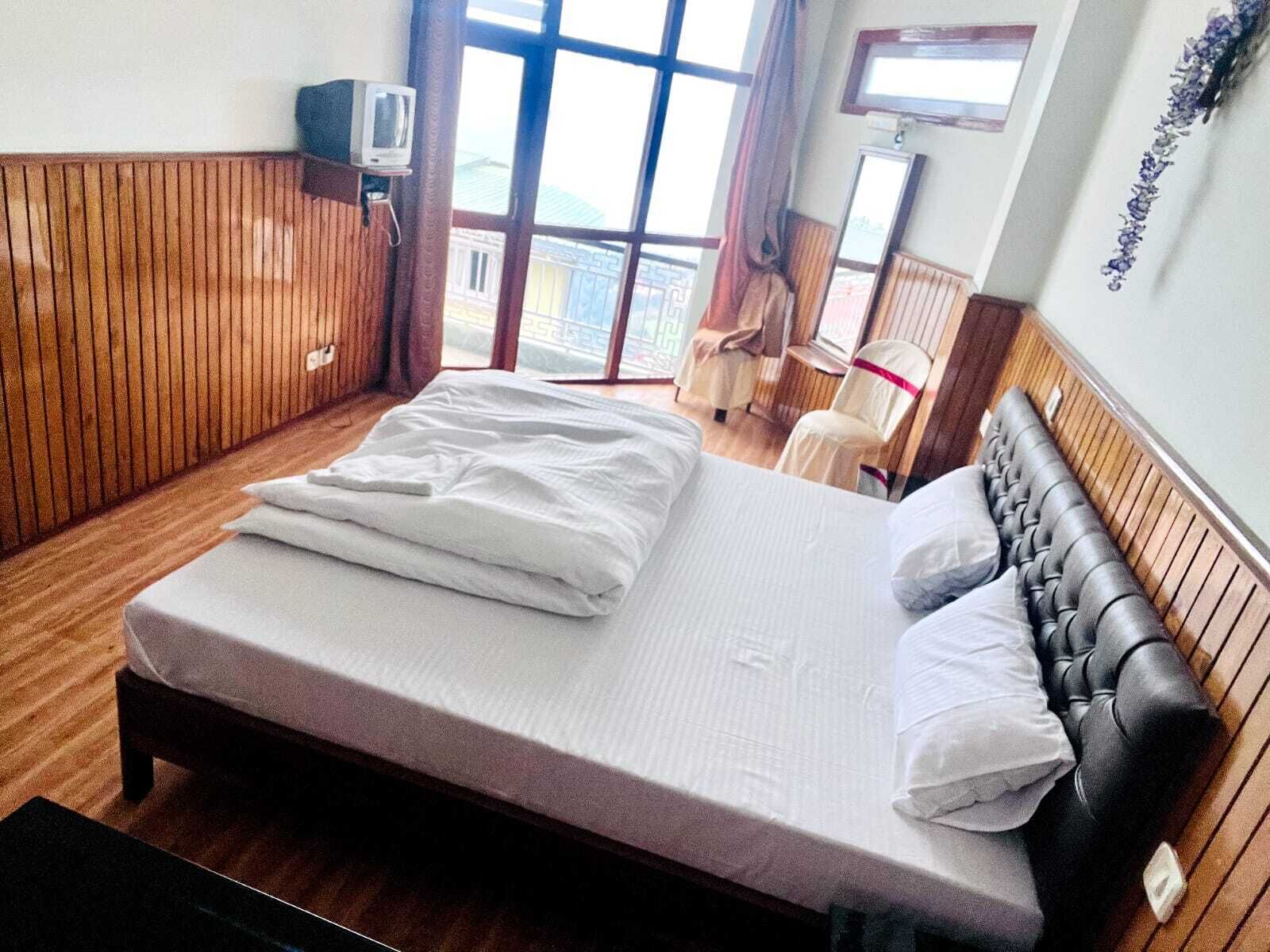 A bedroom with a bed, wooden paneling, a television, and a view through a large window.