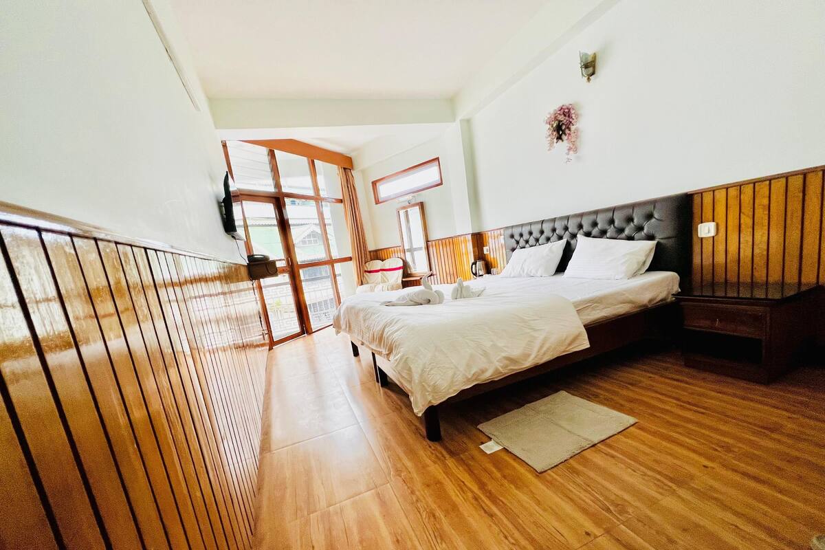 Quarto com cama grande, piso de madeira, varanda e vista para o exterior.