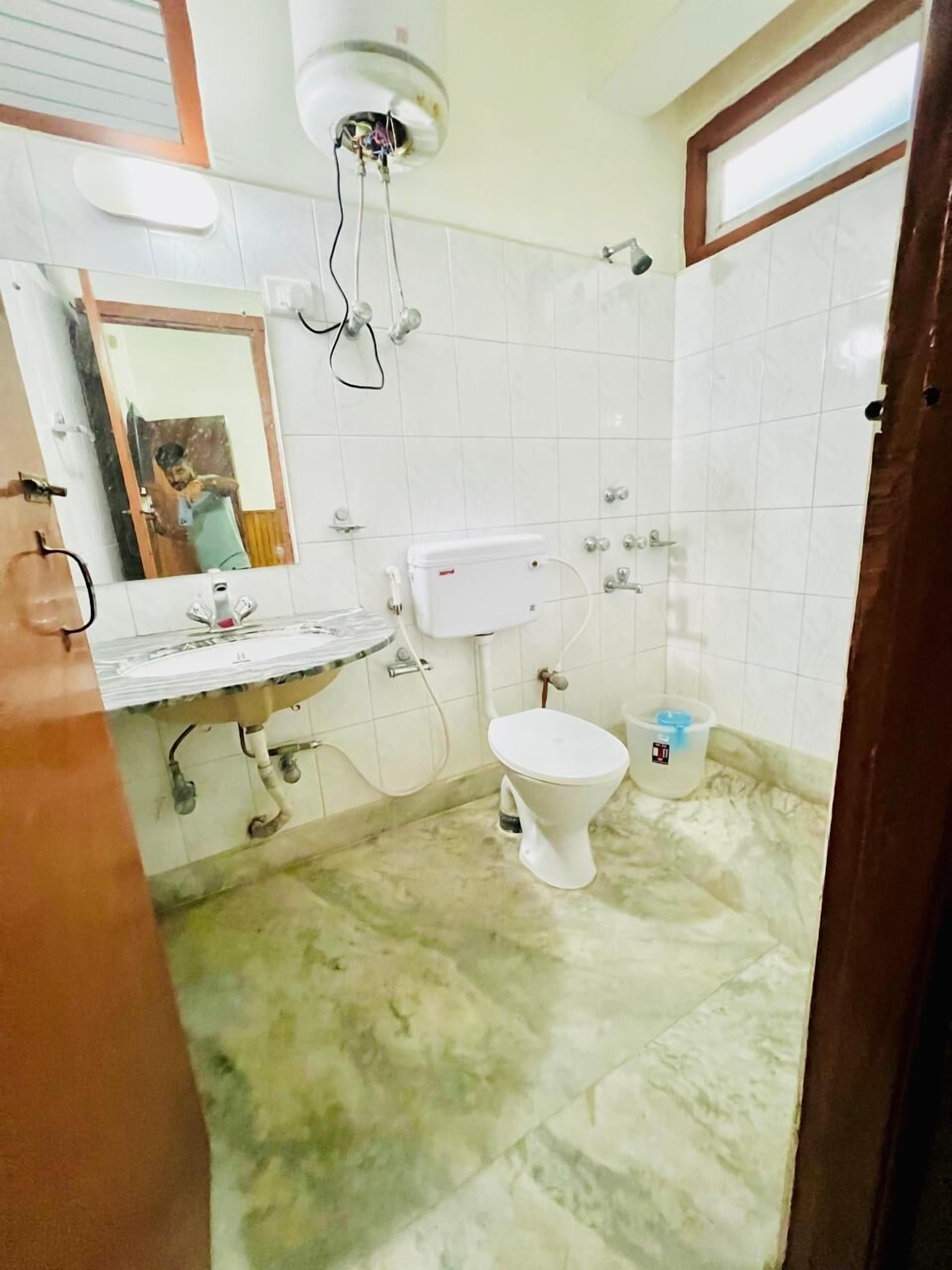 A bathroom with a toilet, sink, mirror, and a ceiling-mounted water heater.