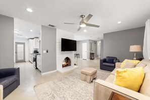 A modern living room with a fireplace, a ceiling fan, and a flat-screen TV mounted on the wall. - 4BR Indio Home | Private Pool, Fire Pit & BBQ (Indio)
