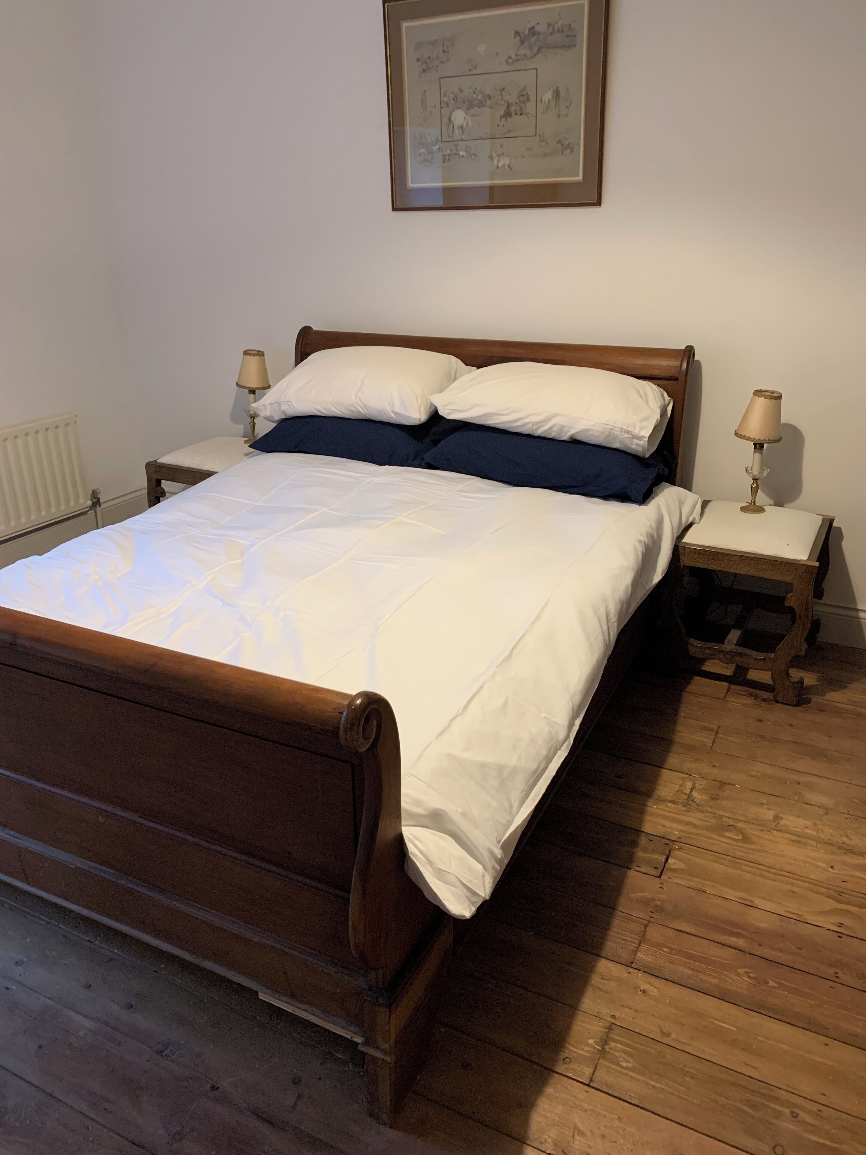 Un lit en bois avec une literie blanche et bleue, deux tables de chevet avec des lampes et un tableau encadré au mur.