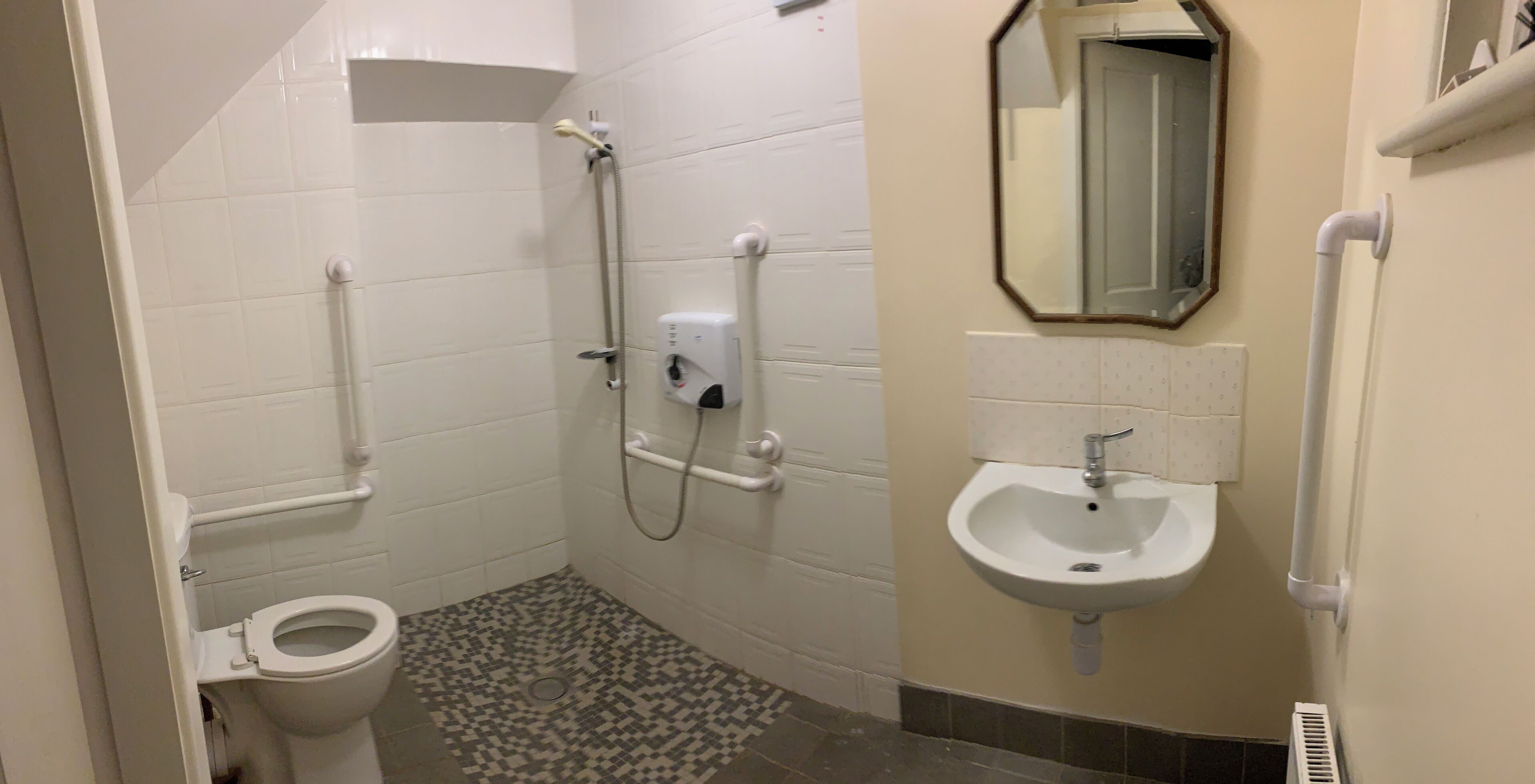 A small bathroom with a toilet, a shower with a handheld showerhead, a sink with a mirror, and a tiled floor.