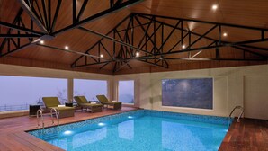 Une piscine intérieure dotée d’une terrasse en bois, de chaises longues et d’une grande fenêtre donnant sur un paysage magnifique.