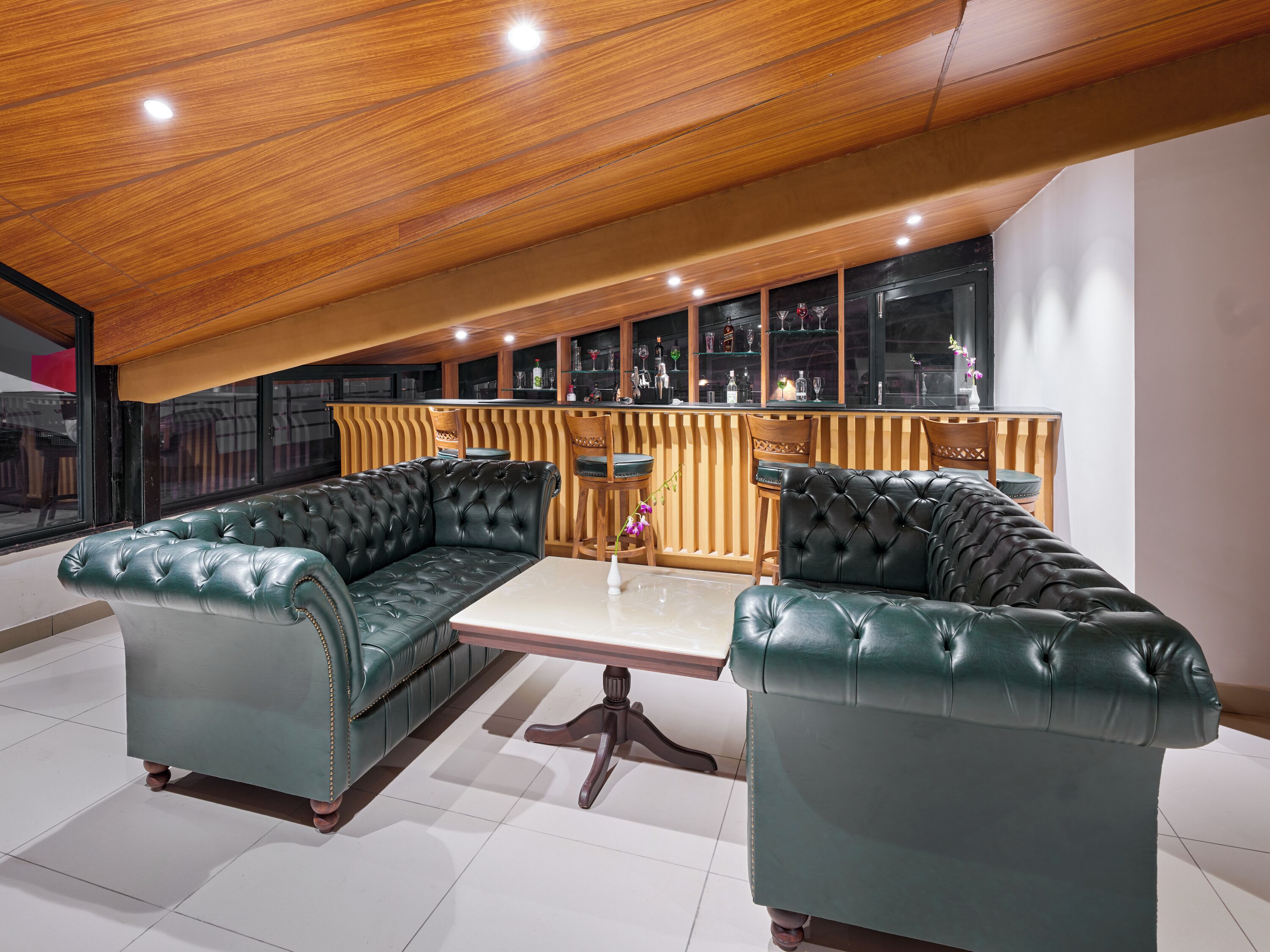 Un área de lounge moderna con sofás de cuero, techo de madera y una barra con estantes de vidrio.