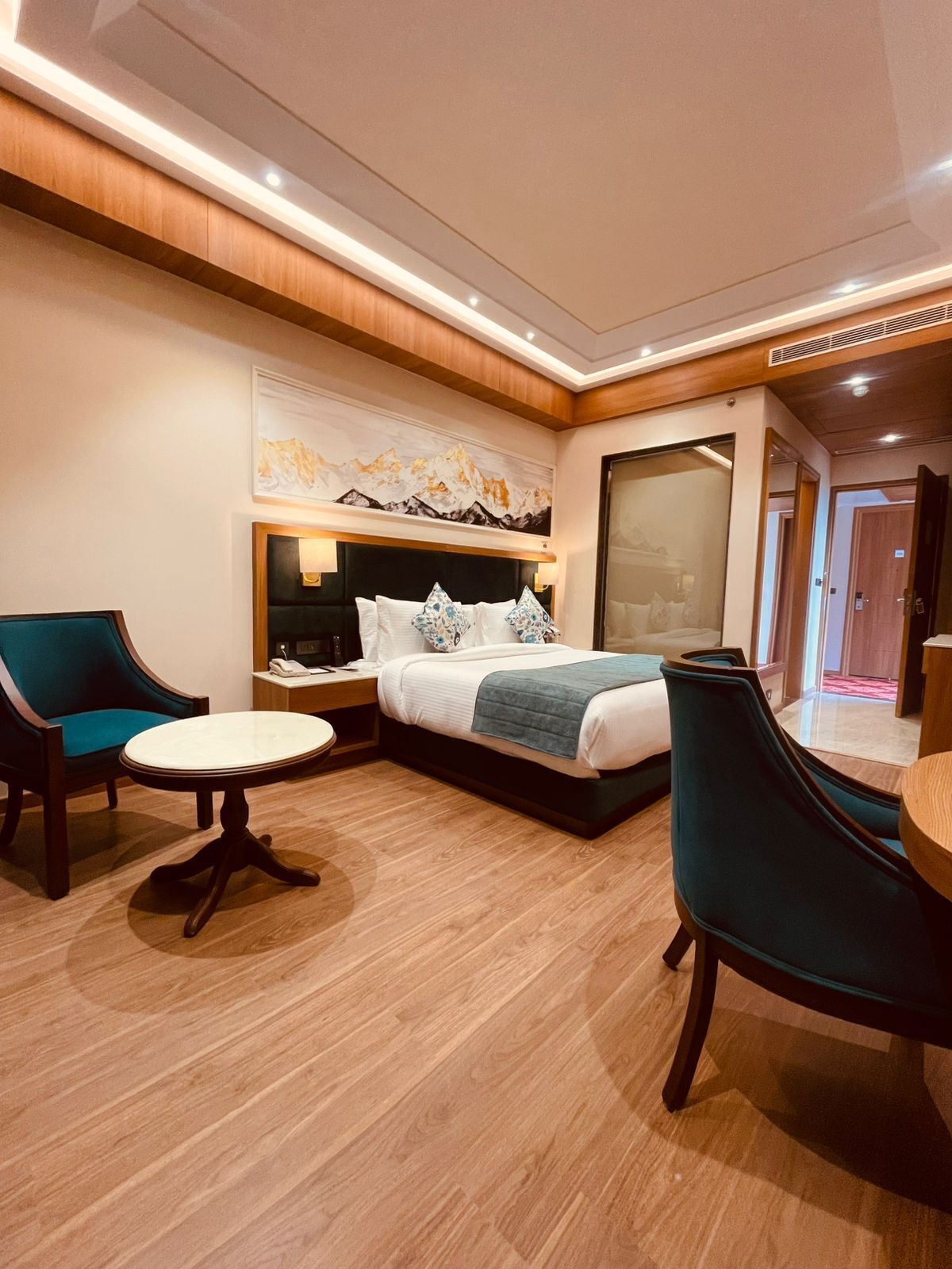 A hotel room with a bed, two chairs, a small table, and a painting on the wall.