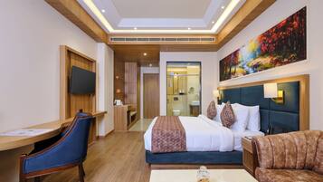 Une chambre d’hôtel avec un lit, un bureau, une chaise, un canapé, une table basse avec des pâtisseries et un tableau au mur.