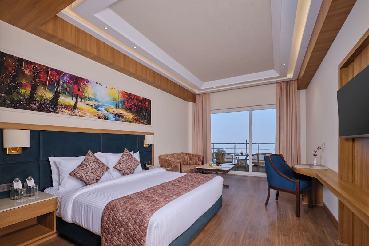 A hotel room with a large bed, a desk, a chair, and a balcony with a view.