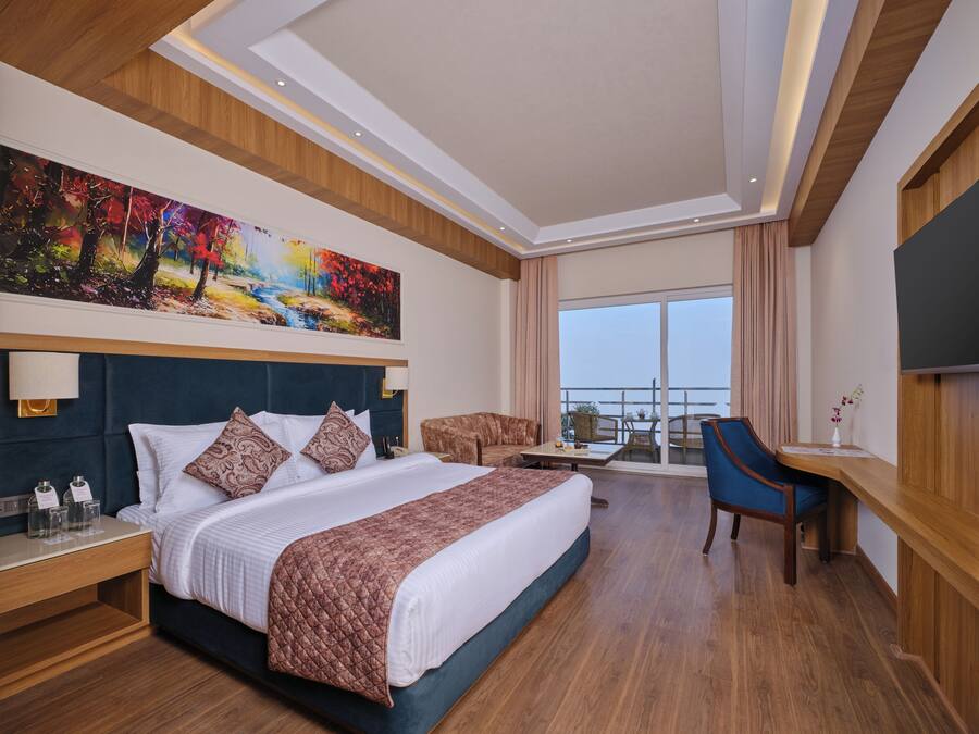 A hotel room with a large bed, a desk, a chair, and a balcony with a view.