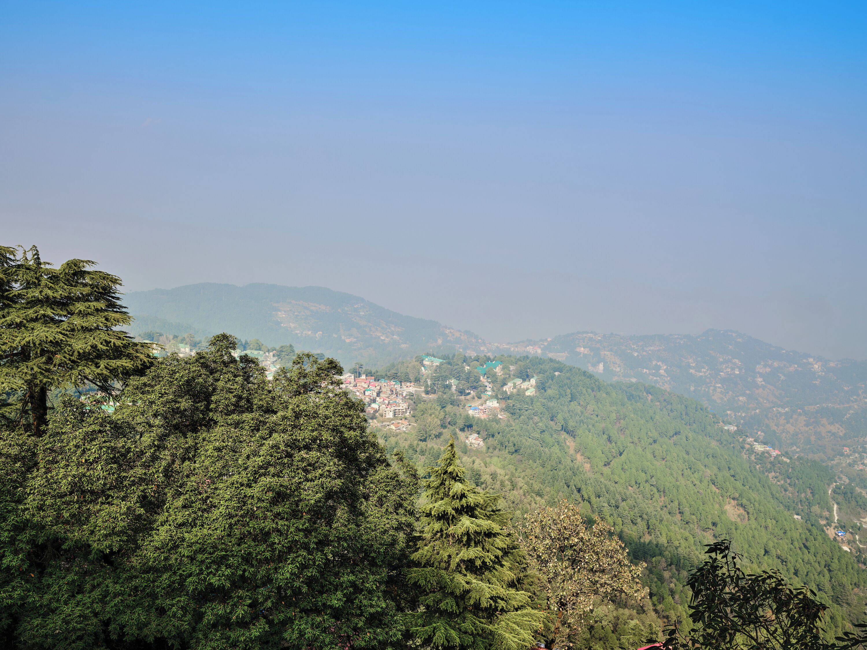 A mountainous landscape with dense forest and a small settlement in the valley.
