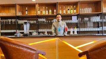 A bar area with shelves of bottles and glasses, a counter with a blender, and leather chairs.