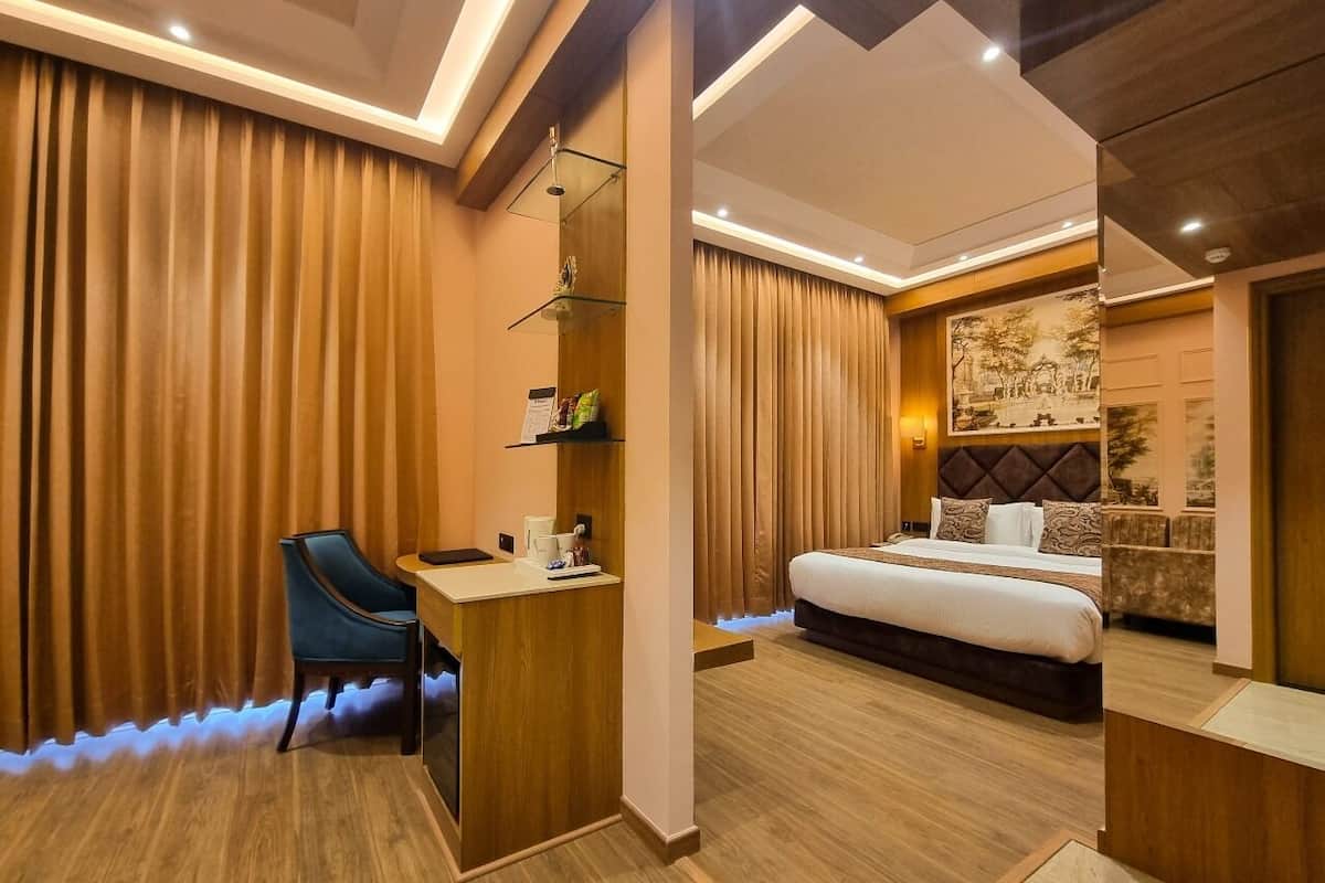 A hotel room with a wooden desk, a bed with a headboard, and a wall-mounted shelf with items.