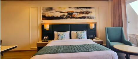 A hotel room with a large bed, a desk, a chair, and a painting on the wall.